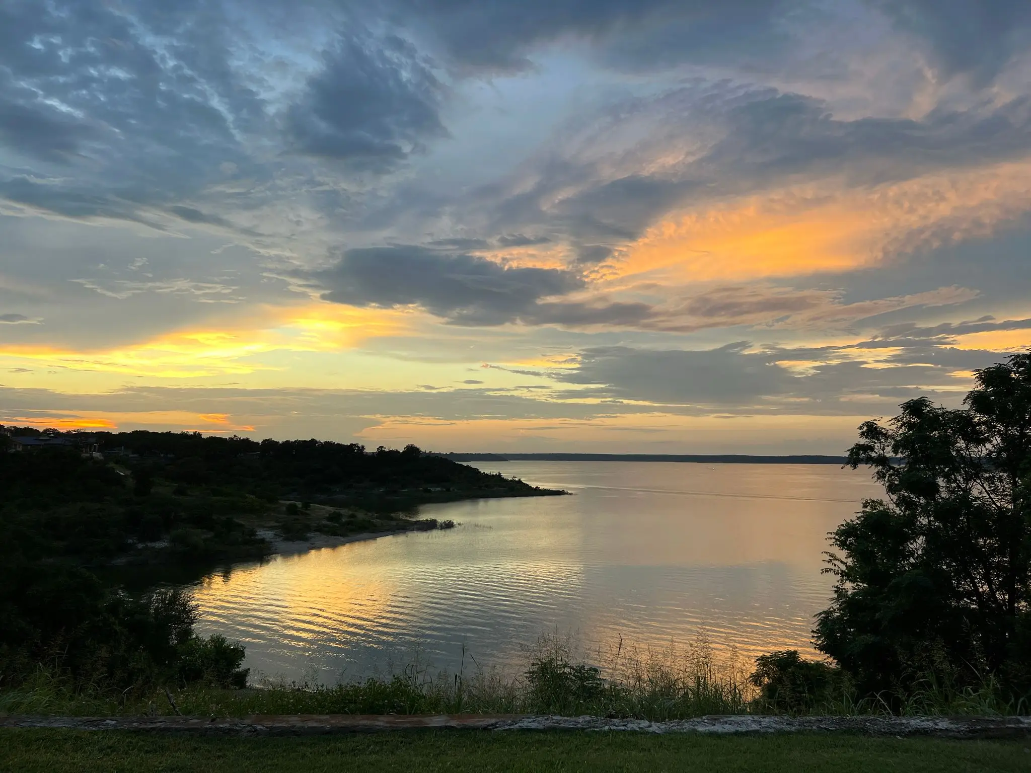 A serene sunset over a calm lake with cloudy skies.